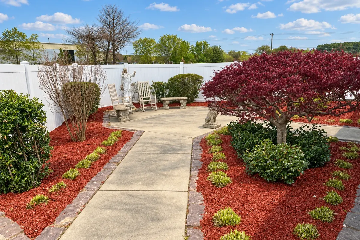 The church prayer garden with a Japanese maple, red mulch, walking paths, seating, and a statue of Jesus